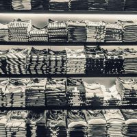 Black and white image showcasing neatly folded t-shirts stacked on store shelves.